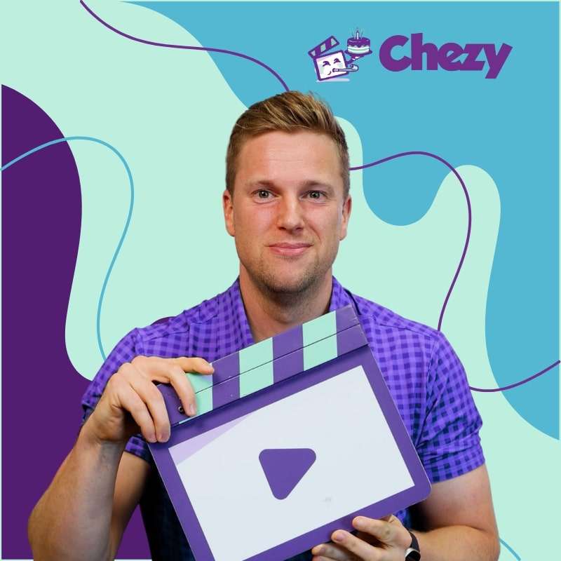 Man holding a Chezy clapperboard in front of a teal and purple background